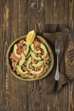 Overhead view of salad with fresh salmon, avocado and onion served in a wooden bowl on a rustic