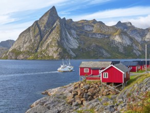 Rorbuer in Hamnoy, fishing boat in front of the mountain Olstinden, blue sky, Moskenesoya, Lofoten,