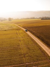 A car on a long dirt road, surrounded by vast golden fields in autumnal scenery, electric car VW