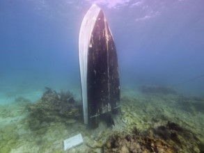 An upright boat underwater, surrounded by sand and coral, in a tranquil atmosphere, dive site John