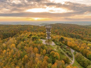 Sunlight bathes the observation tower and the surrounding autumn forest in vibrant colours,