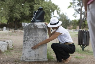 Woman explaining ancient inscriptions on a stone, archaeological site of Olympia, UNESCO World