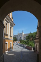 View through an archway to a medieval-style castle under a blue sky, view through the Grodzka Tor