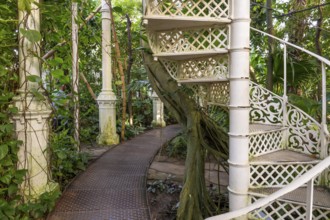 Decorative white spiral staircase and cast iron columns amidst lush vegetation, historic