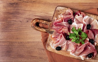 Sliced prosciutto, on a cutting board, with olives and herbs, snack, breakfast, no people