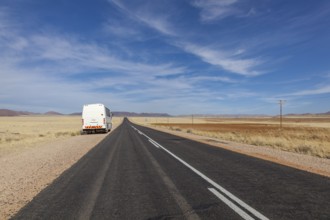 A bus on a deserted country road through a wide, dry landscape under a blue sky, national road B4