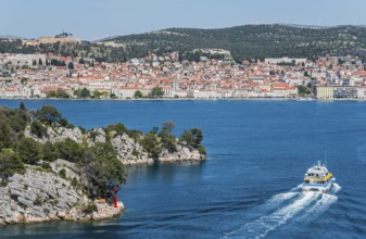 A boat moves through the blue water with a view of a built-up coastal landscape, St Anthony's