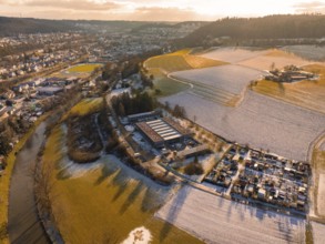 Winter aerial view of a river and neighbouring fields with snow-covered landscape at sunset,