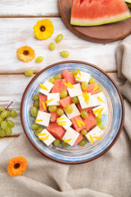 Vegetarian salad with watermelon, feta cheese, and grapes on blue ceramic plate on white wooden