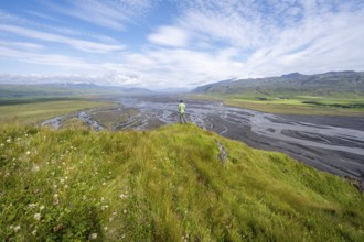 Hiker, young man on a hill, view over alluvial land, meandering river, Dímonarhellir, Suðurland,