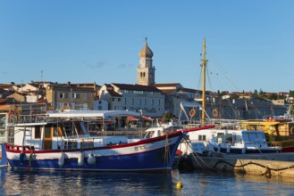 A harbour full of boats and ships with a striking bell tower in the background under a sunny sky,