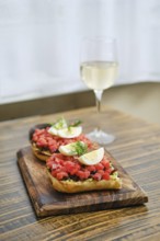 A wooden serving board holds two generous portions of bruschetta topped with diced salmon and egg