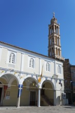 White church building with a high bell tower against a clear blue sky in a city setting, Holy