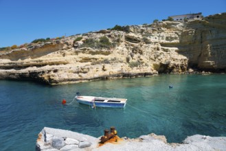 Lonely boat on calm water in front of high rocks under a clear sky, Mezapos, Mani, Peloponnese,