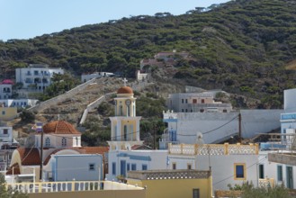 Mediterranean village of Diafani with church tower and houses on a wooded hill, hiking trail from