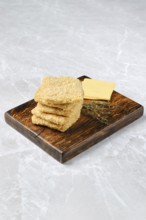 Homemade cheese crackers are neatly stacked on a rustic wooden board. Fresh thyme sprigs accompany