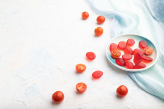 Jelly tomato candies on white concrete background and blue linen textile. copy space, side view