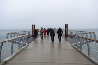 A gloomy day at a pier with several people looking towards the sea, Prerow pier,