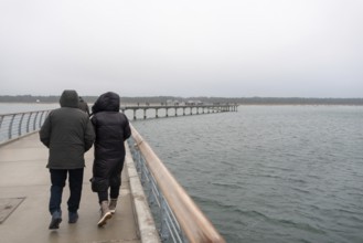 A couple walks along the new pier in rainy weather, Prerow, Mecklenburg-Vorpommern, Germany, Europe