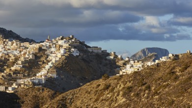 An elongated village under a bright sky with scattered clouds, situated on a hill, Colourful