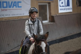 Little girl, 10 years old, in the saddle on a horse in an indoor riding arena,