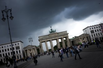 People visit the Brandenburg Gate on a day with a threatening, dramatic sky and heavy clouds, a