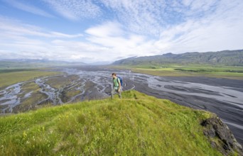 Hiker, young man on a hill, view over alluvial land, meandering river, Dímonarhellir, Suðurland,