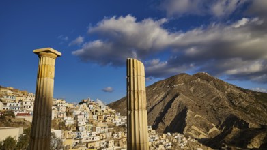 Ancient columns stand in front of a village that blends into an impressive mountain landscape,