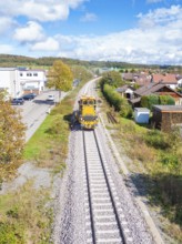 Maintenance vehicle on the railway tracks, surrounded by houses and under a cloud cover, tamping