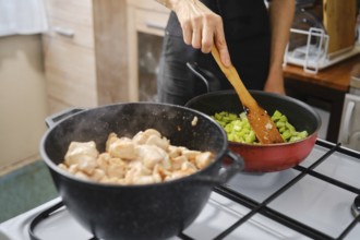 A person stirs vegetables in a red pan on the stove making the base for chicken ragout