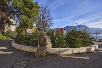 Christmas market in Piazza Manzoni, roundabout with Christmas trees, lake, mountains, trees, blue