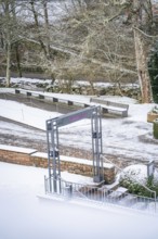 A quiet park in winter with snow-covered paths, trees and an empty bench, spa garden, Bad Wildbad,