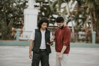 Portrait of two smiling guys using cell phone outdoors. Two happy friends using the mobile phone on