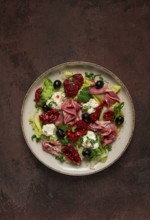 Salad with dried tomatoes, prosciutto, soft cheese, olives, homemade, top view