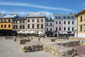 Row of historic houses and stone benches on a sunny square, foundations of St Michael's parish