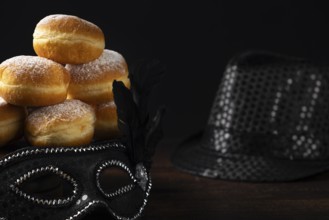 Doughnuts against a dark background next to a black hat and carnival mask