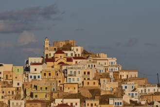 Close-up of a stack of colourful houses on a hill, a prominent tower above in the morning light,