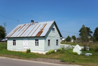 Small green wooden house with metal shingle roof and garden in a quiet rural setting, house and dog