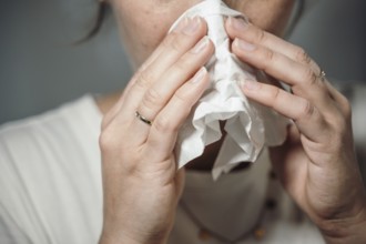 Woman holding a crumpled handkerchief to her nose, possibly with a cold or sneezing, 'symbolic