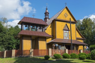 Yellow wooden church with bell tower and red roof, surrounded by trees and sky, Church of the Holy