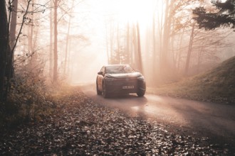 A car on a foggy road in autumn forest with golden sunlight in the morning, electric car VW ID5,