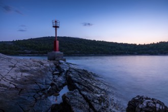 Lighthouse or red sea mark on a rocky coast at dusk, surrounded by gentle waves, Hvar, Dalmatia,