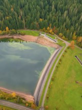 View from above of a dam wall with surrounding lake and forest in a colourful autumn landscape,