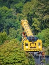 Yellow crane from Leonhard Weiss works on a railway line, embedded in a green and wooded natural