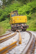 Yellow train runs on winding tracks through a green landscape, track construction, Hermann