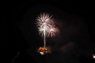 Large fireworks display glows colourfully in the night sky above an illuminated building, New