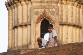 Young man on wall in front of terracotta temple, Bishnupur, Bankura district, West Bengal, India,