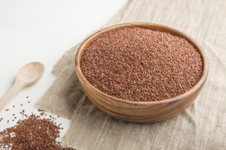 Wooden bowl with raw red quinoa seeds on a white wooden background and linen textile. Side view,