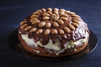 Homemade chocolate cake with milk cream and almonds on black wooden background. close up