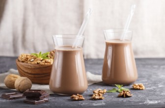 Organic non dairy walnut chocolate milk in glass and wooden plate with walnuts on a black concrete